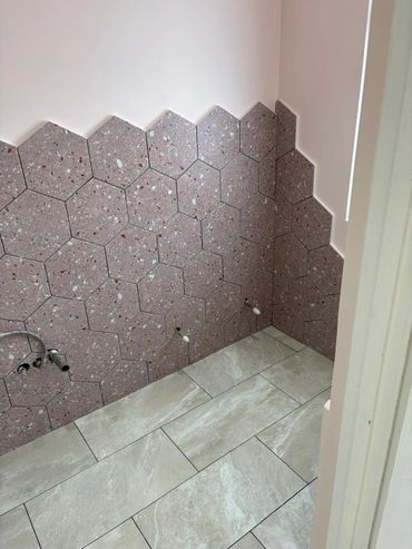 Bathroom wall with hexagonal tiles and light floor tiles in progress.