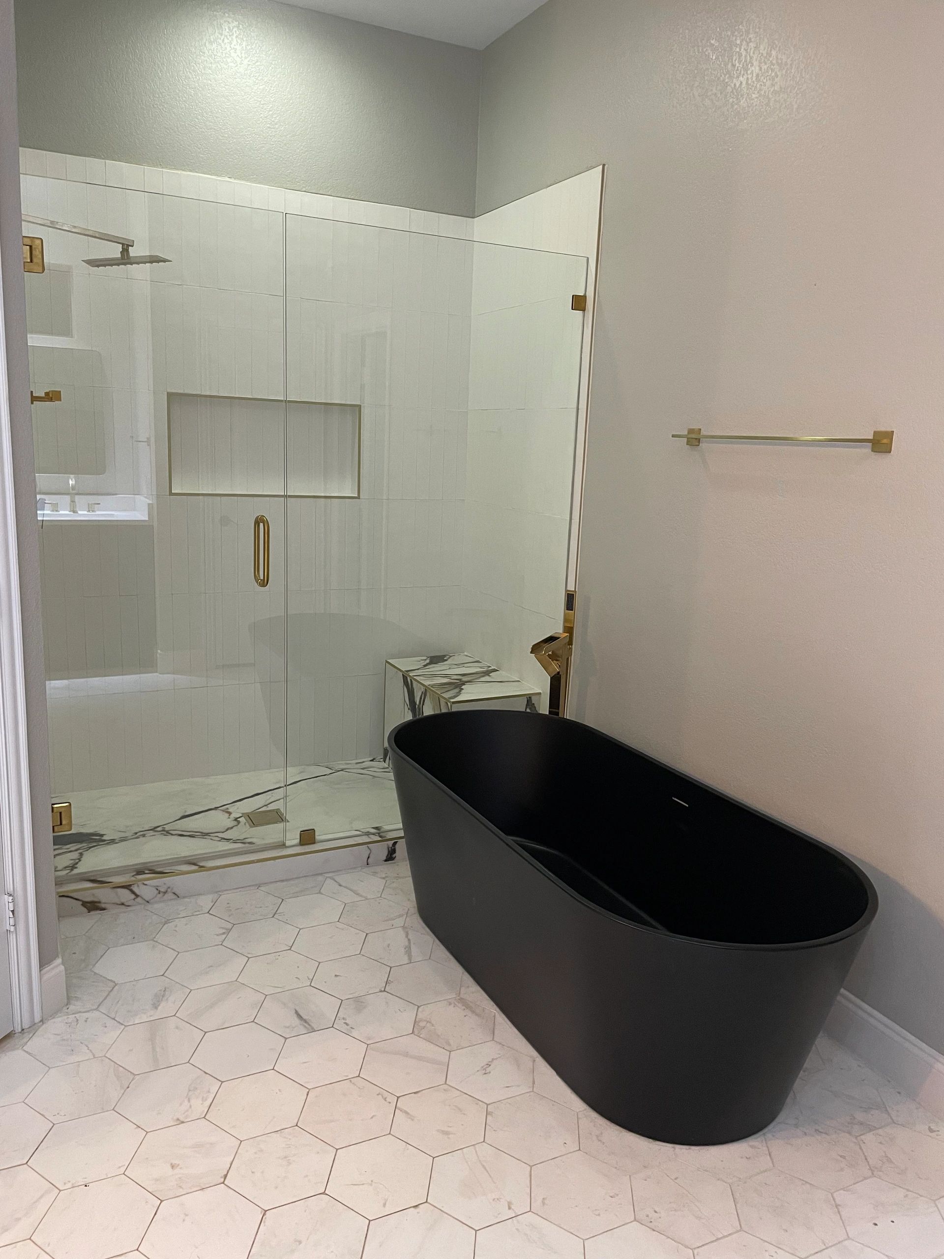 Modern bathroom with black bathtub and glass shower enclosure.