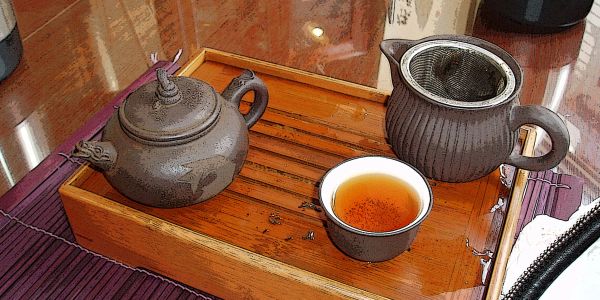 Traditional tea set with teapot, cup, and strainer on wooden tray.