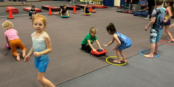 Children playing and exercising on mats and hoops indoors.