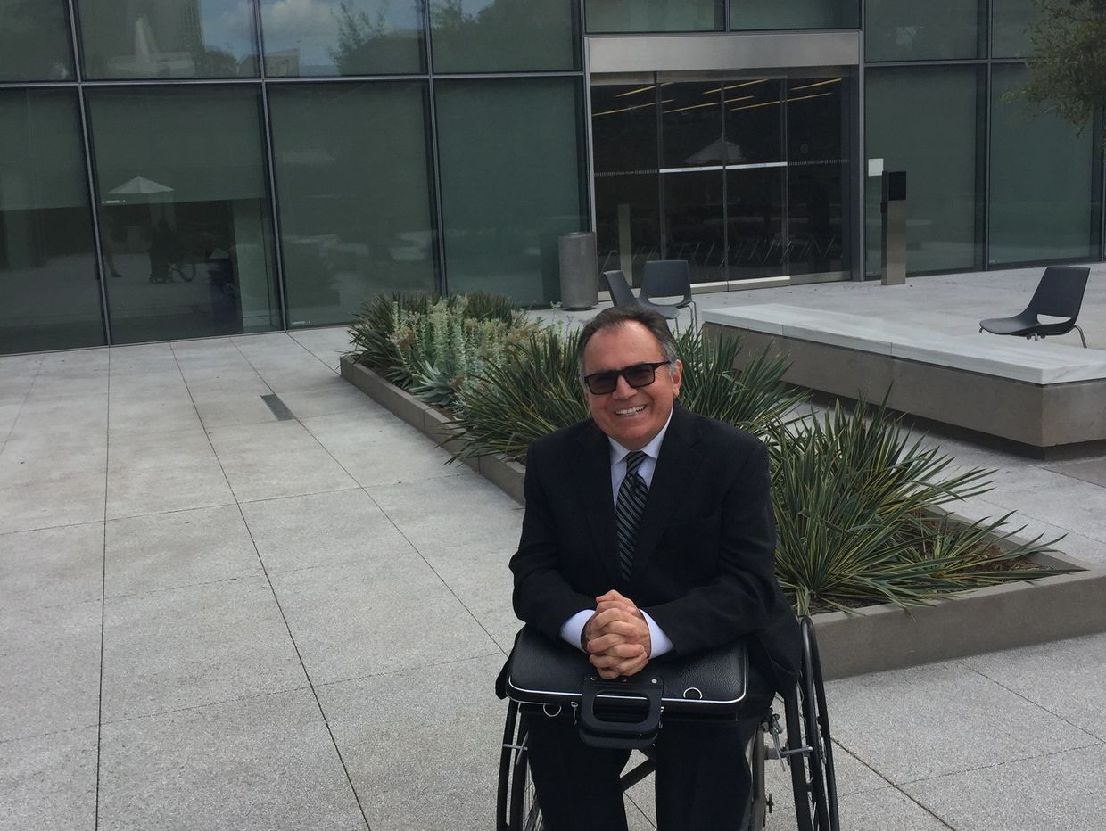 Man in a wheelchair wearing a suit and smiling outdoors.