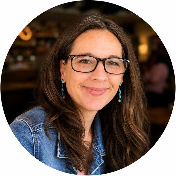 Smiling woman in glasses and denim jacket.