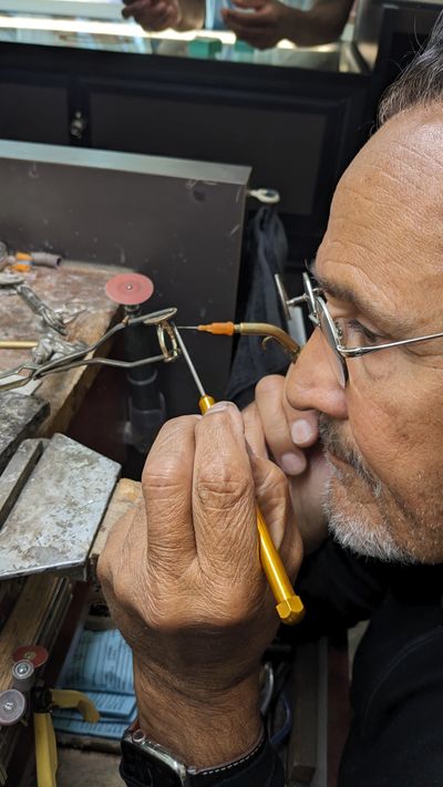A craftsman carefully works on a small metal piece with precision tools.