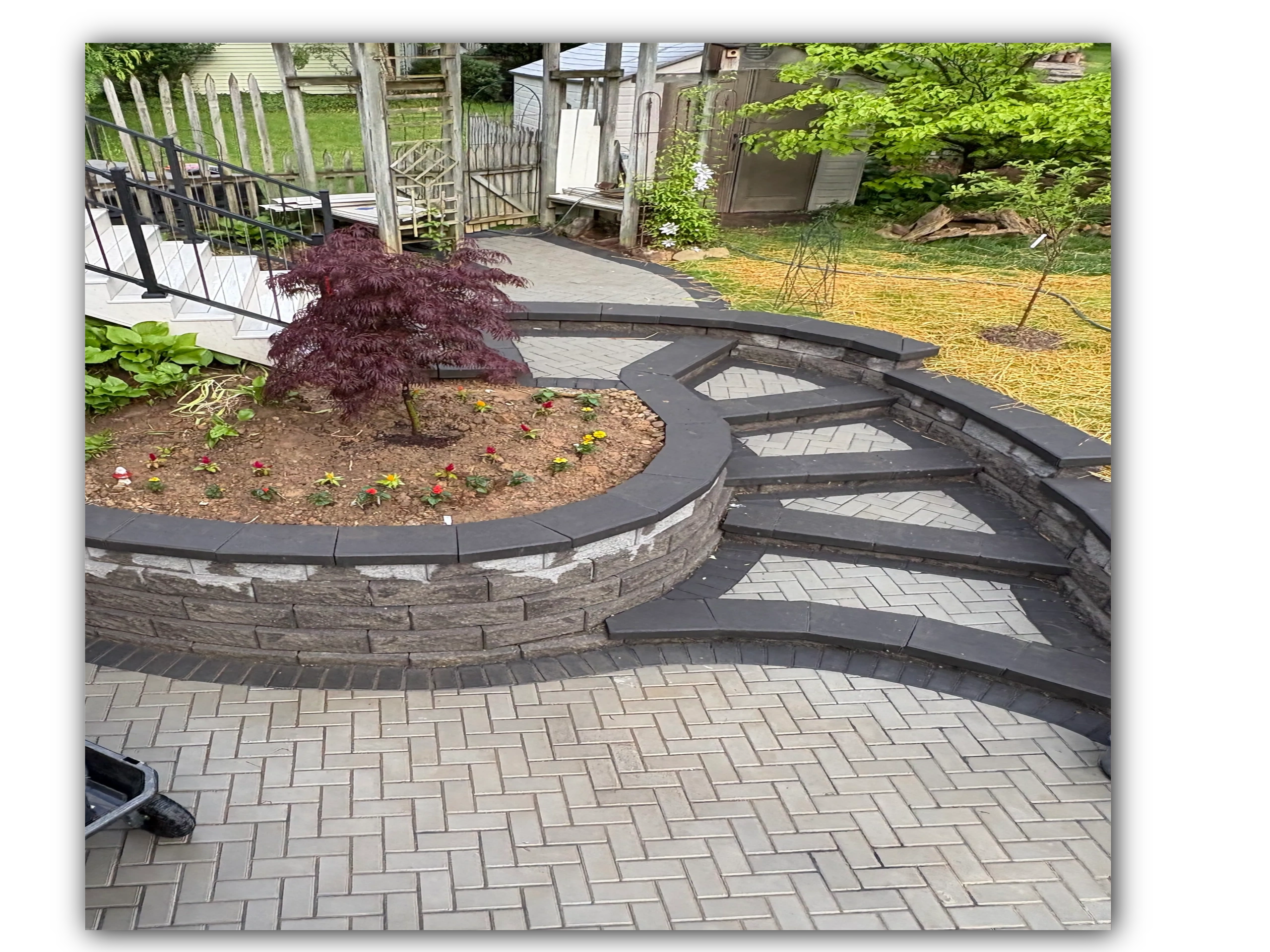 A curved retaining wall and steps leading to a garden with a landscaping and paver patio