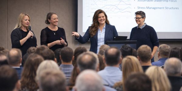 Four women presenting to an audience in a conference room.