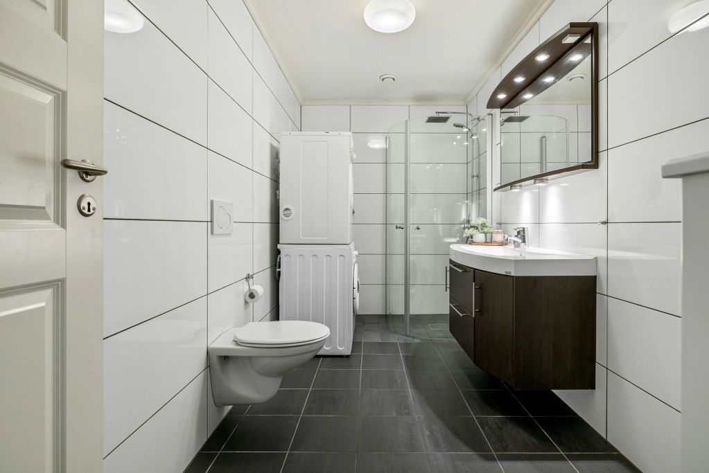 Moderne badkamer met wit tegelwerk en donkere vloer.