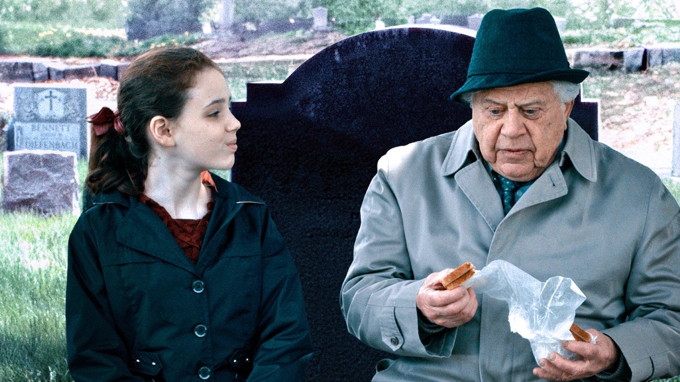 An image of a girl and an elderly man sitting in a cemetery.