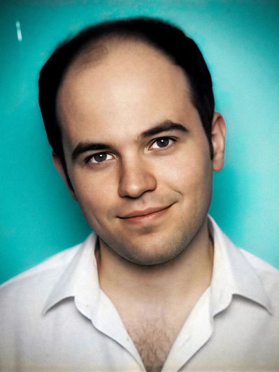 Headshot of filmmaker Max Hechtman in a white shirt, standing in front of a teal backdrop.