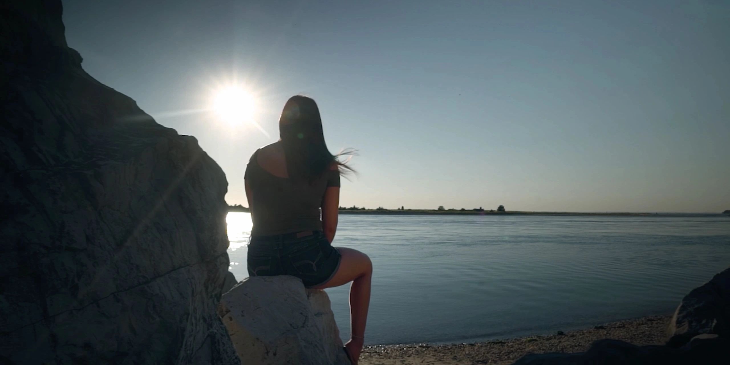 An image of a girl in silhouette on a rock watching the sunset on the beach.