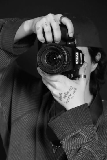 Person holding a Canon camera, taking a photo, with handwritten notes on their hand.