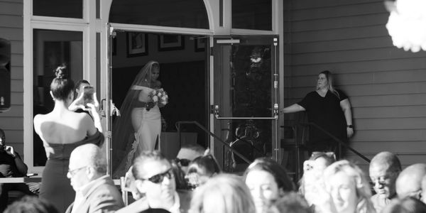 Bride steps out holding flowers, guests watch and capture the moment.