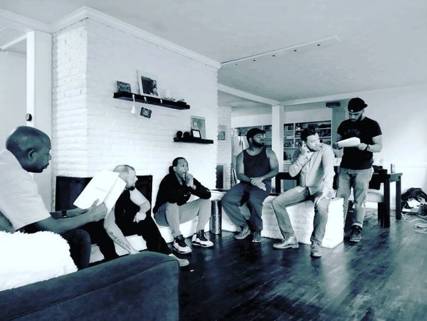 Group of men engaged in a script reading or discussion in a living room.