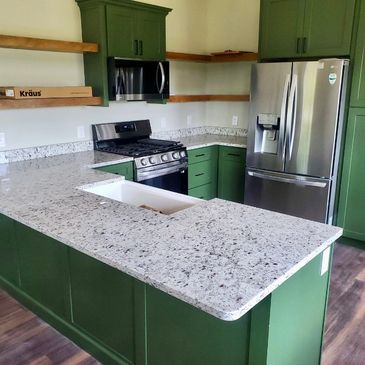 A kitchen with green cabinets and white granite countertops.