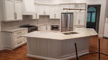 A kitchen with cream cabinets and beige quartzite countertops, with full height stone backsplash.