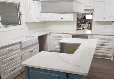 A kitchen with white perimeter cabinets with blue island cabinets and white quartz countertops