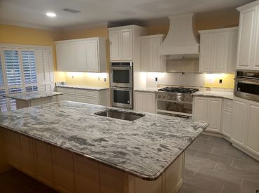 A kitchen with white cabinets and gray and white veined countertops.