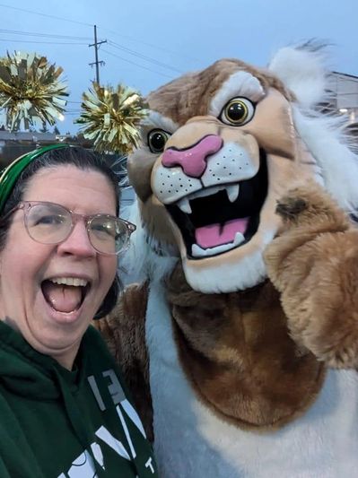 Woman posing excitedly with a lion mascot outdoors.