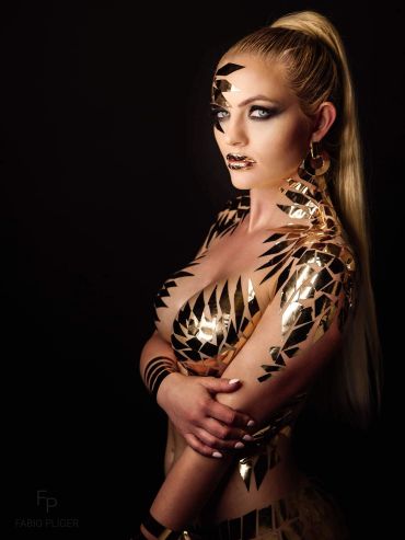 Woman covered in geometric gold and black body paint against a black background.