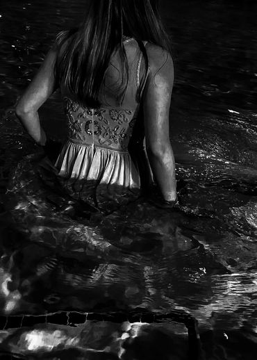 Black and white image of a person wading through water. 