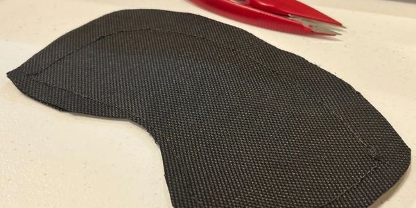 Black fabric piece with stitching on a white surface, red scissors in background.