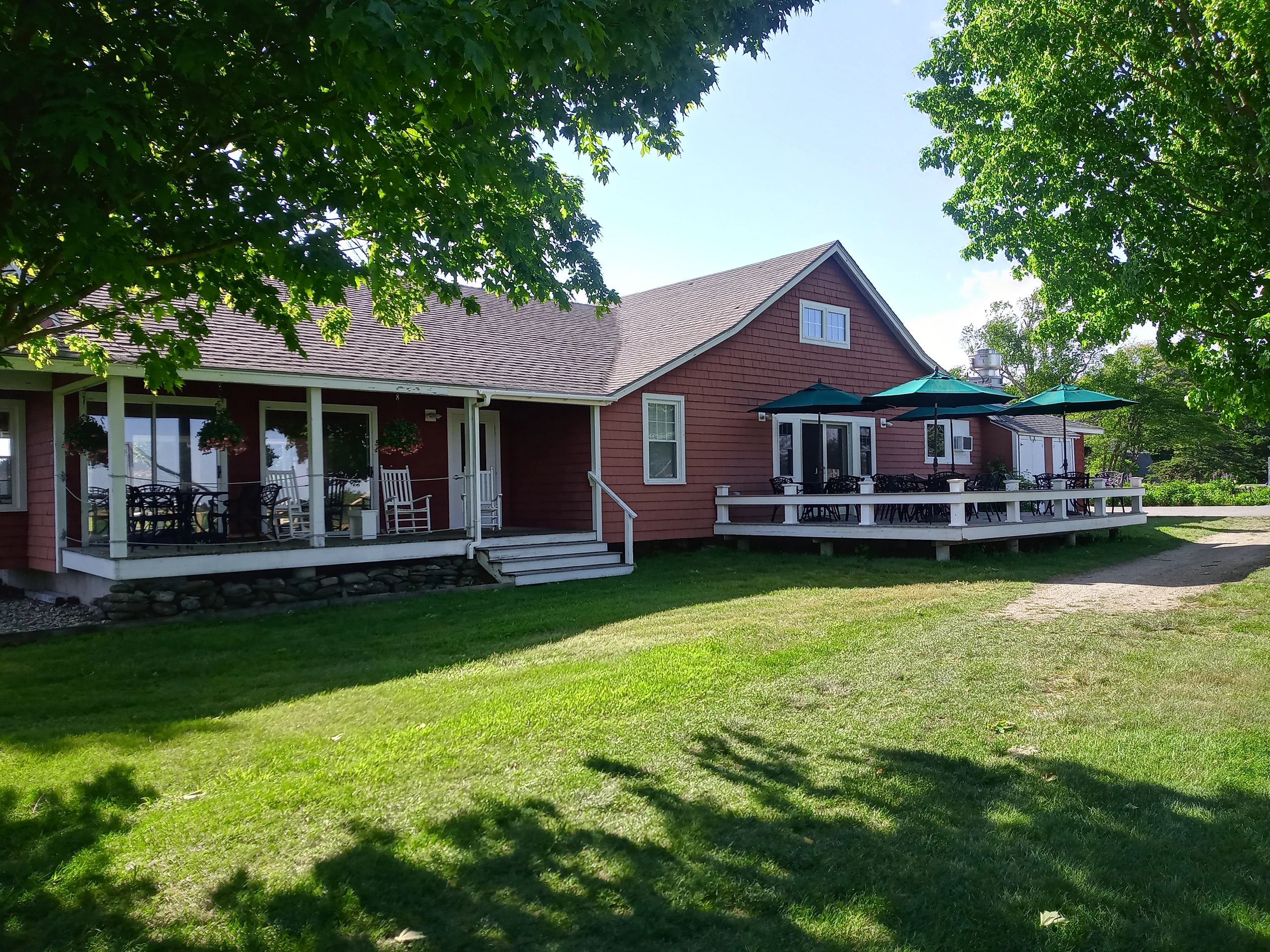 Red house with porch and outdoor seating under green trees on a sunny day.