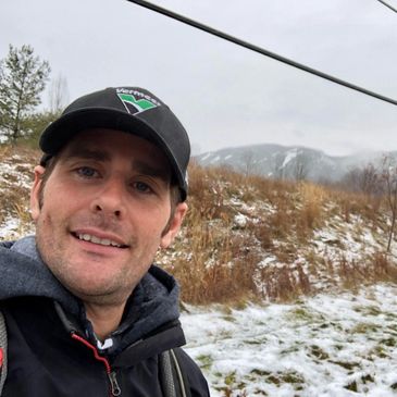 Man in outdoor winter setting with light snow and mountains in the background.
