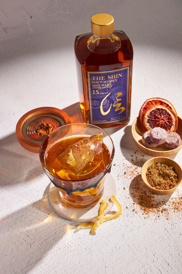 Whiskey bottle and glass with ice, garnishes, and spices.