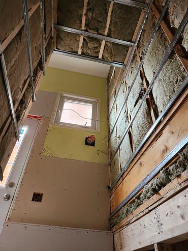 Interior wall under renovation with exposed insulation and wiring.