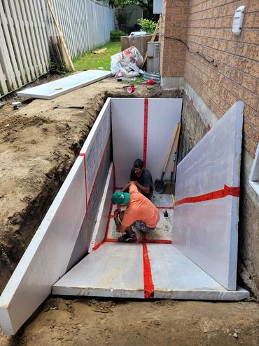 Two workers installing waterproof panels in a basement excavation.