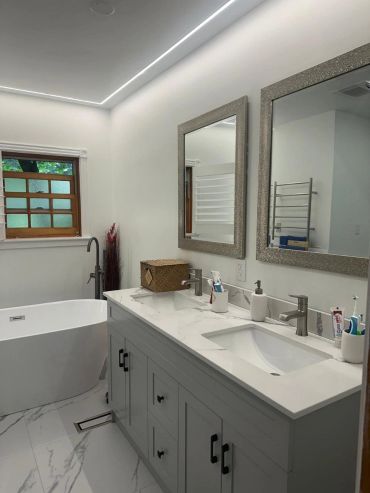 Modern white bathroom with dual sinks and a bathtub.