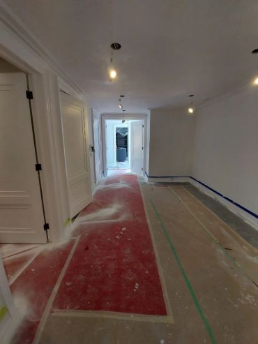 Hallway under construction with taped floors and exposed lights.