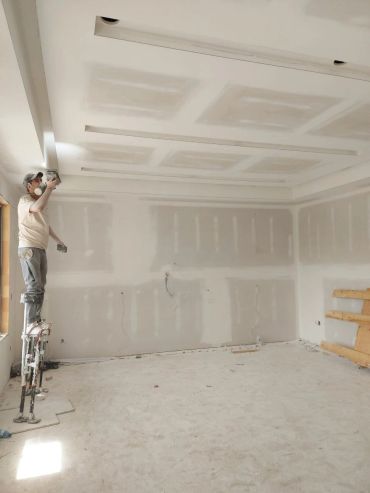 Worker standing on stilts applying drywall finishing.
