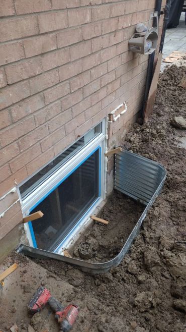 Window well installation beside a brick house.