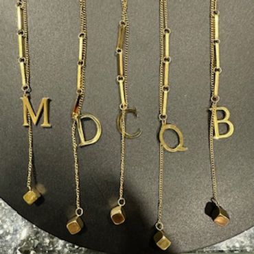 Gold necklaces with letter pendants and small cube charms on a dark background.