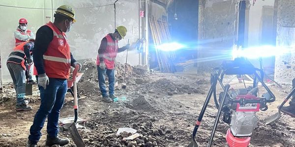 Trabajadores con cascos y chalecos en obra bajo luces.