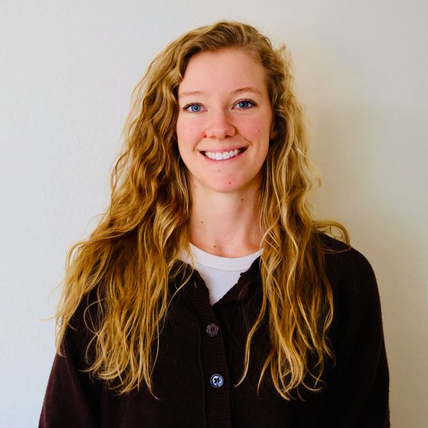 Young woman with long blonde hair smiling against a plain background.