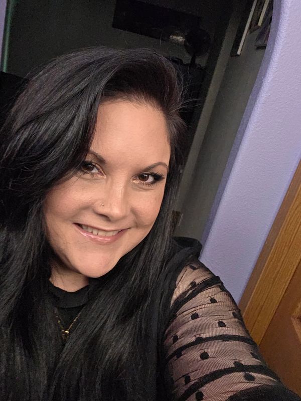 Smiling woman with long black hair wearing a black polka-dot mesh top.