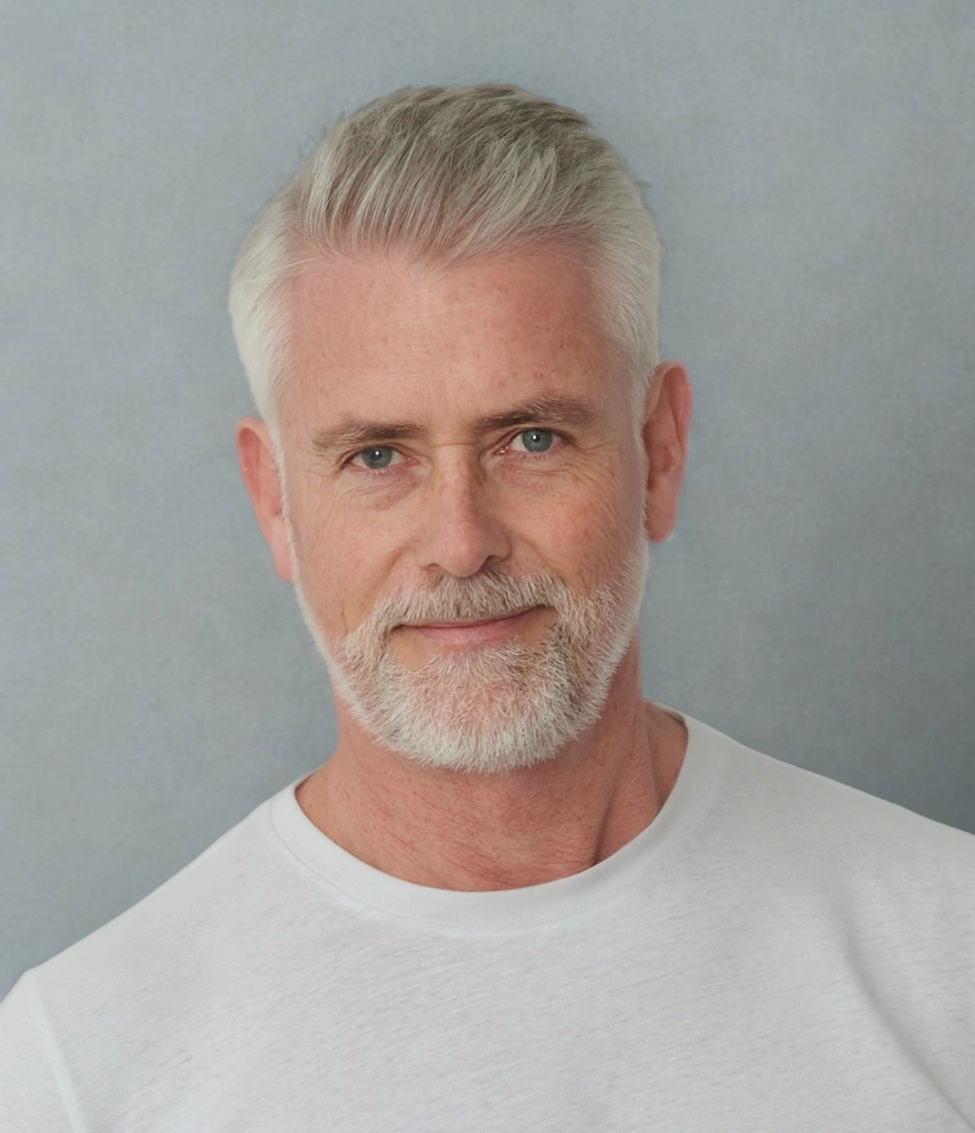 Portrait of a smiling older man with gray hair and beard in a white shirt.