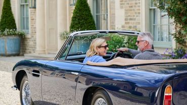 A couple enjoys a drive in a classic blue convertible car.