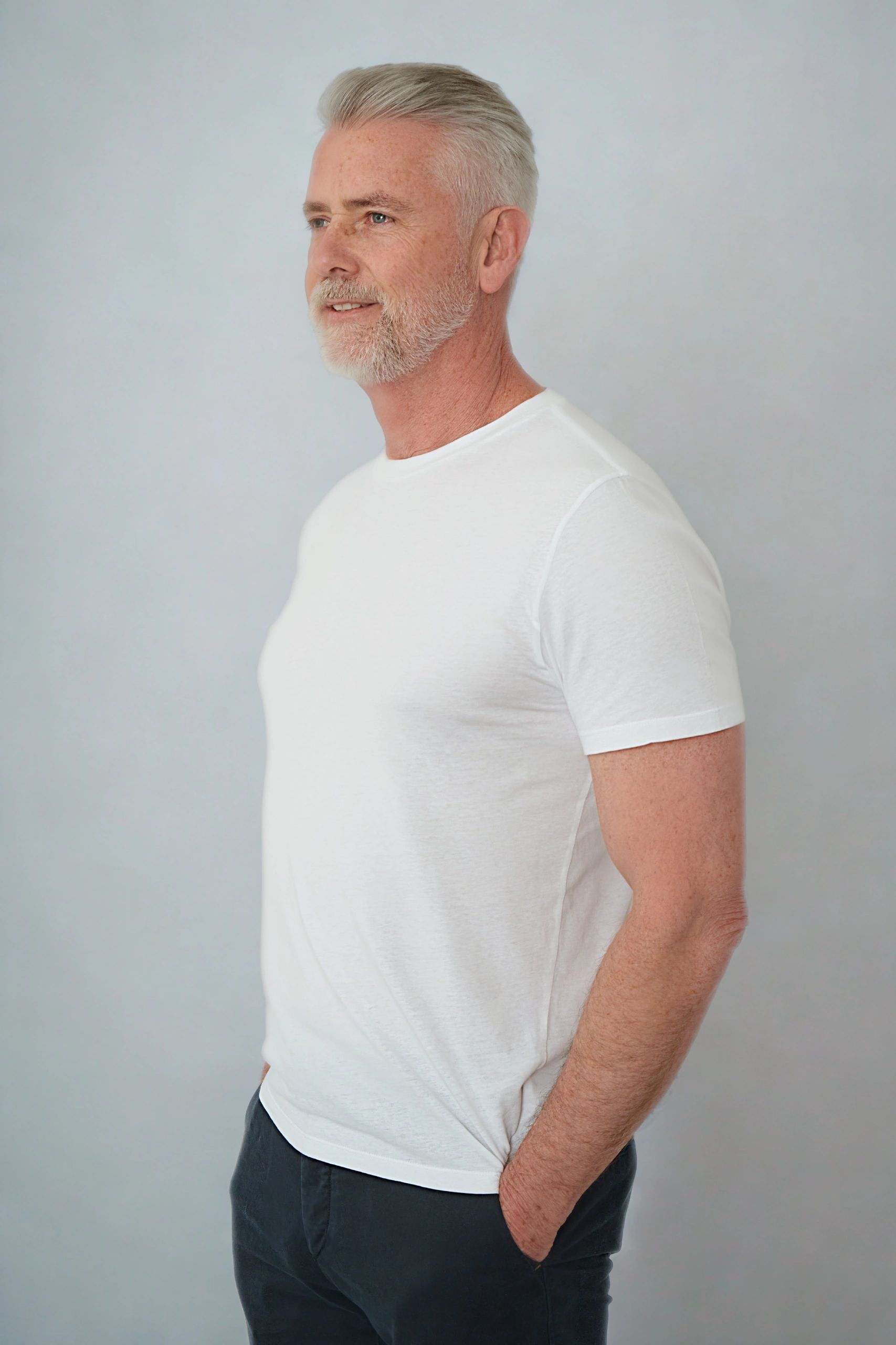 Smiling mature man with gray hair and beard in a white t-shirt.