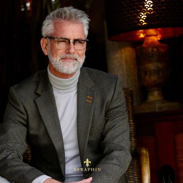 Distinguished older man with gray hair and beard, wearing glasses and a gray suit jacket.