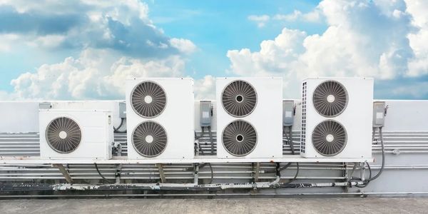 Four white air conditioning units mounted outdoors under a cloudy sky.