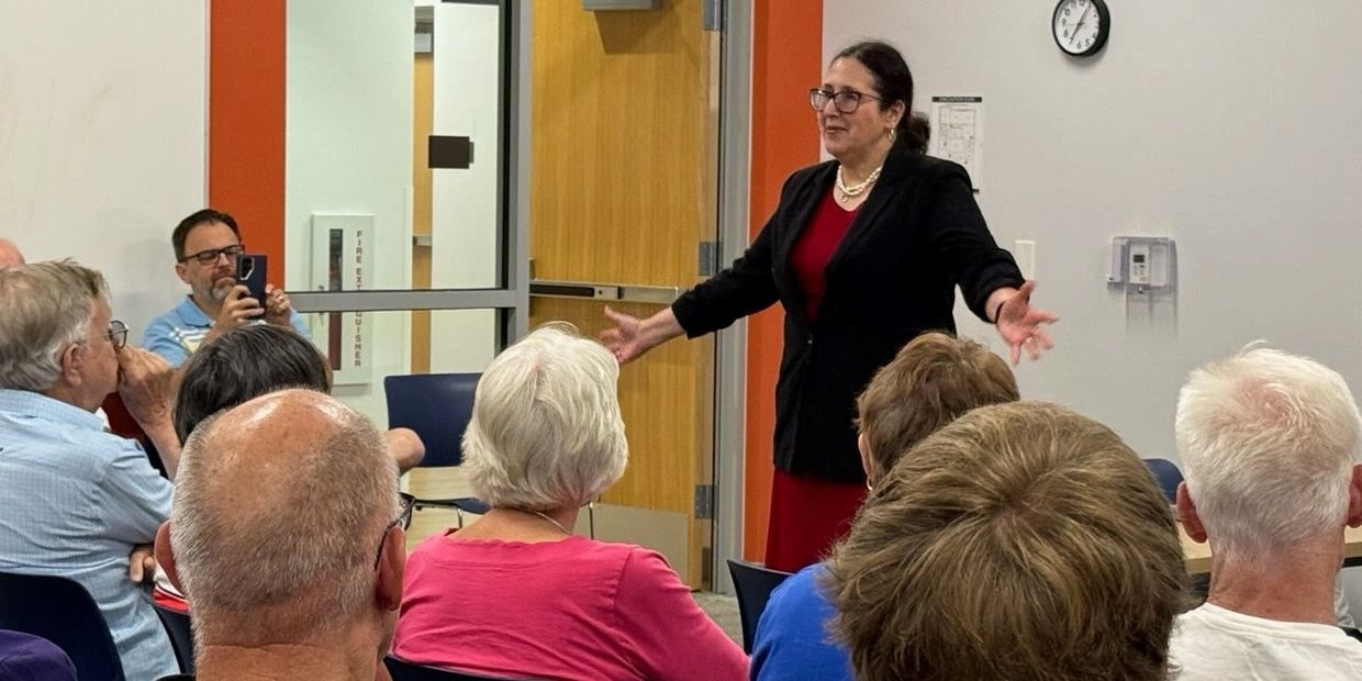Woman speaking to seated audience in a meeting room.