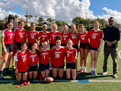 PVISE girls' football team posing on field with two coaches under sunny sky.