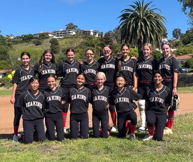 A girls' softball team posing together outdoors in black uniforms.