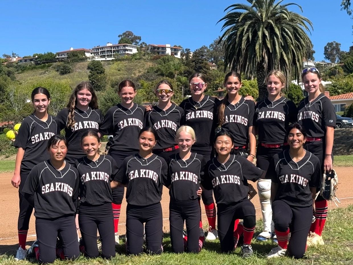 A girls' softball team posing outdoors in matching black Sea Kings uniforms.