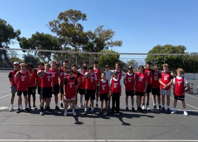 Youth basketball team posing on outdoor court in red jerseys under clear sky.