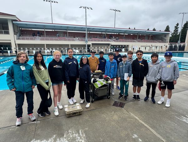 A group of students standing by a pool with robotic equipment.