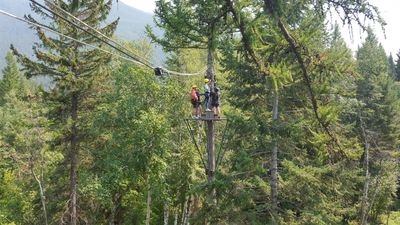 Two people riding a zip line through a forested area.