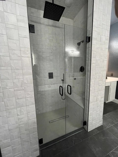 Modern glass shower enclosure with black fixtures and textured white tiles.